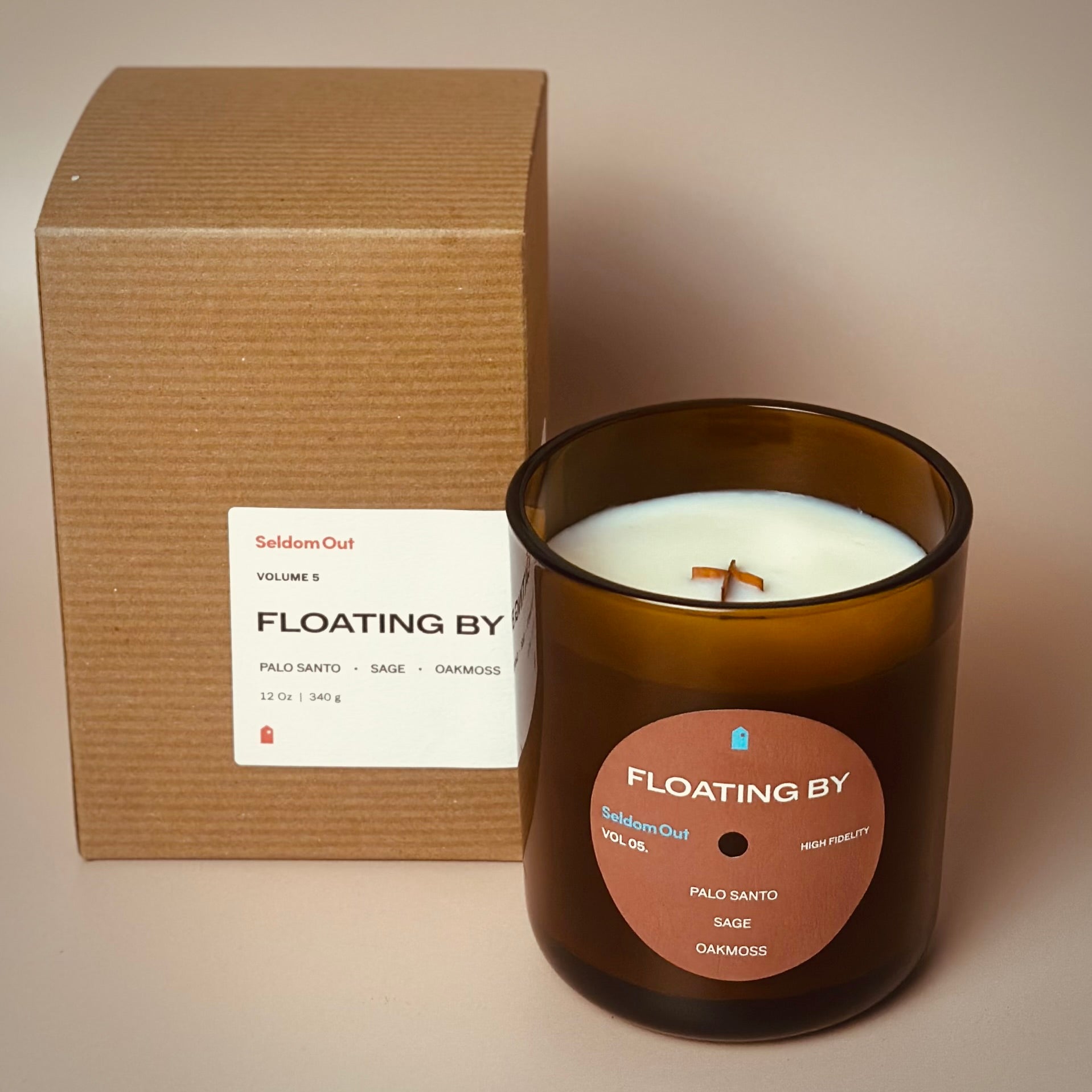 A portrait image of our 12oz Dreamwave candle standing next to its Kraft box packaging. It has a slightly brown tinted glass vessel, a round label with a hole at the center, like a vinyl record.
