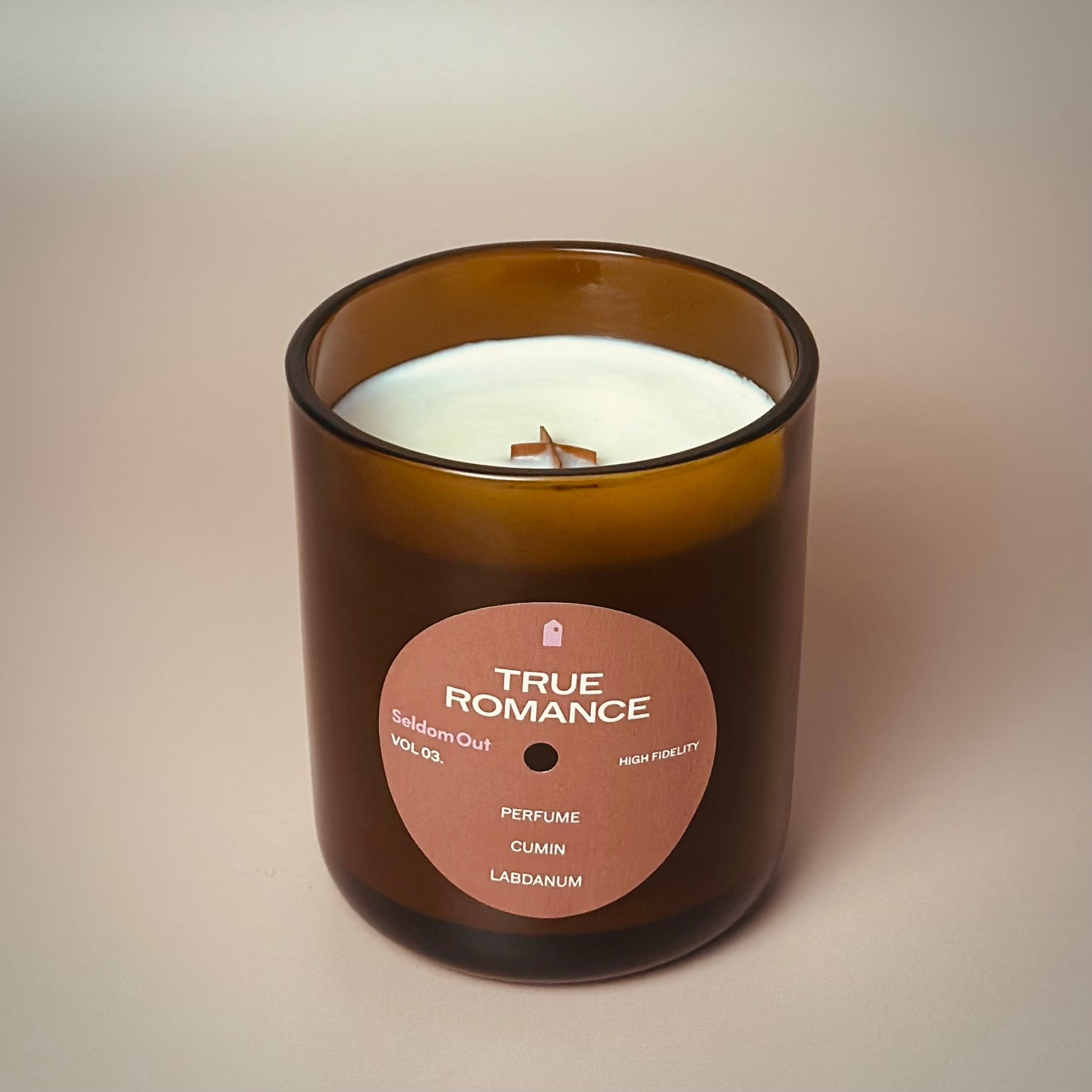 A portrait image of our 12oz True Romance scented candle made in a heavy amber glass jar. It features a round front label, that has a hole cut out in the middle, not unlike a vinyl record.