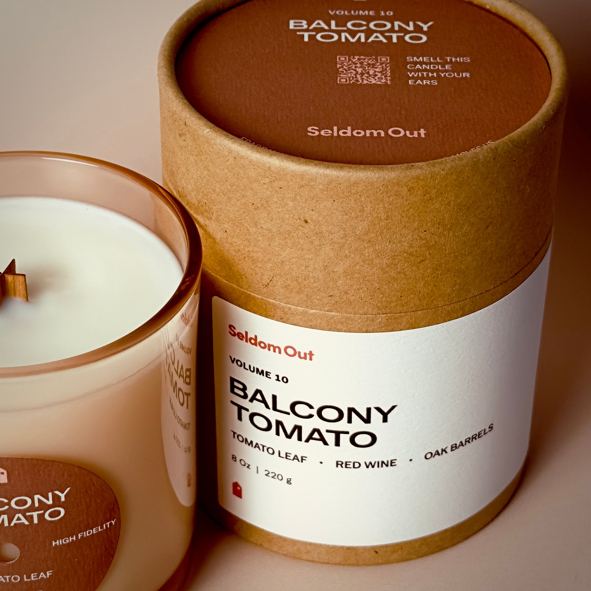 A close up image of our round kraft packaging for our 8oz Balcony Tomato Scented Candle. It features a wide front label, the label on the top has a QR code with the instructions to smell this candle with your ears.