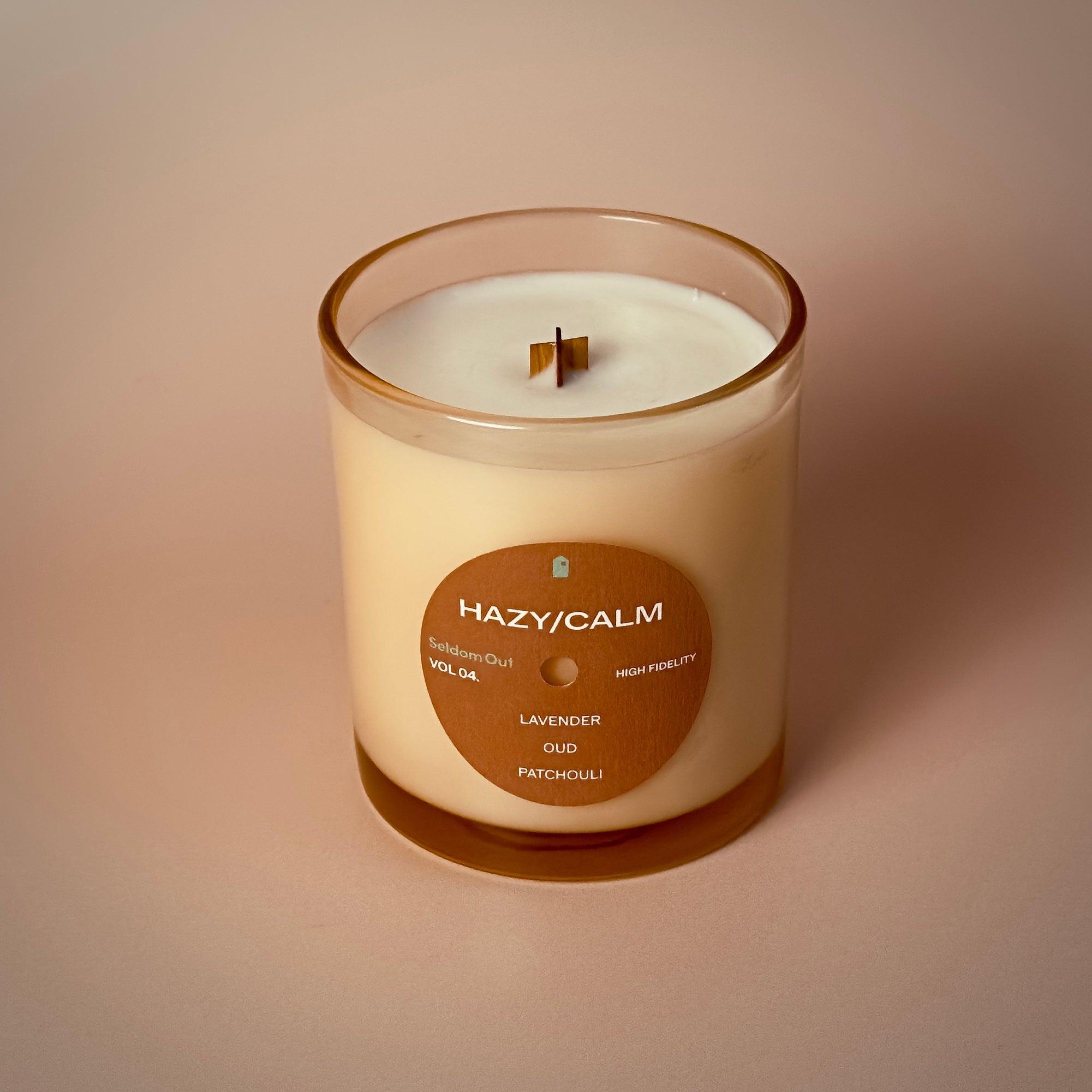 A portrait image of our 8oz Hazy / Calm scented candle. It has a slightly brown tinted glass vessel, a round label with a hole at the center, like a vinyl record.