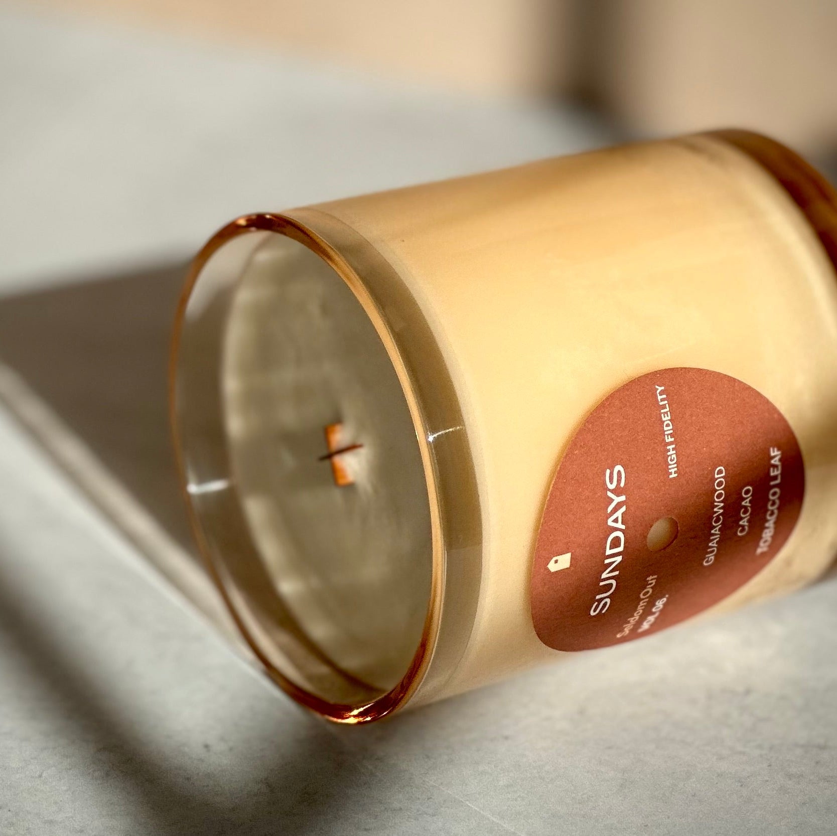 Candle in a tinted glass container with a label on a light surface