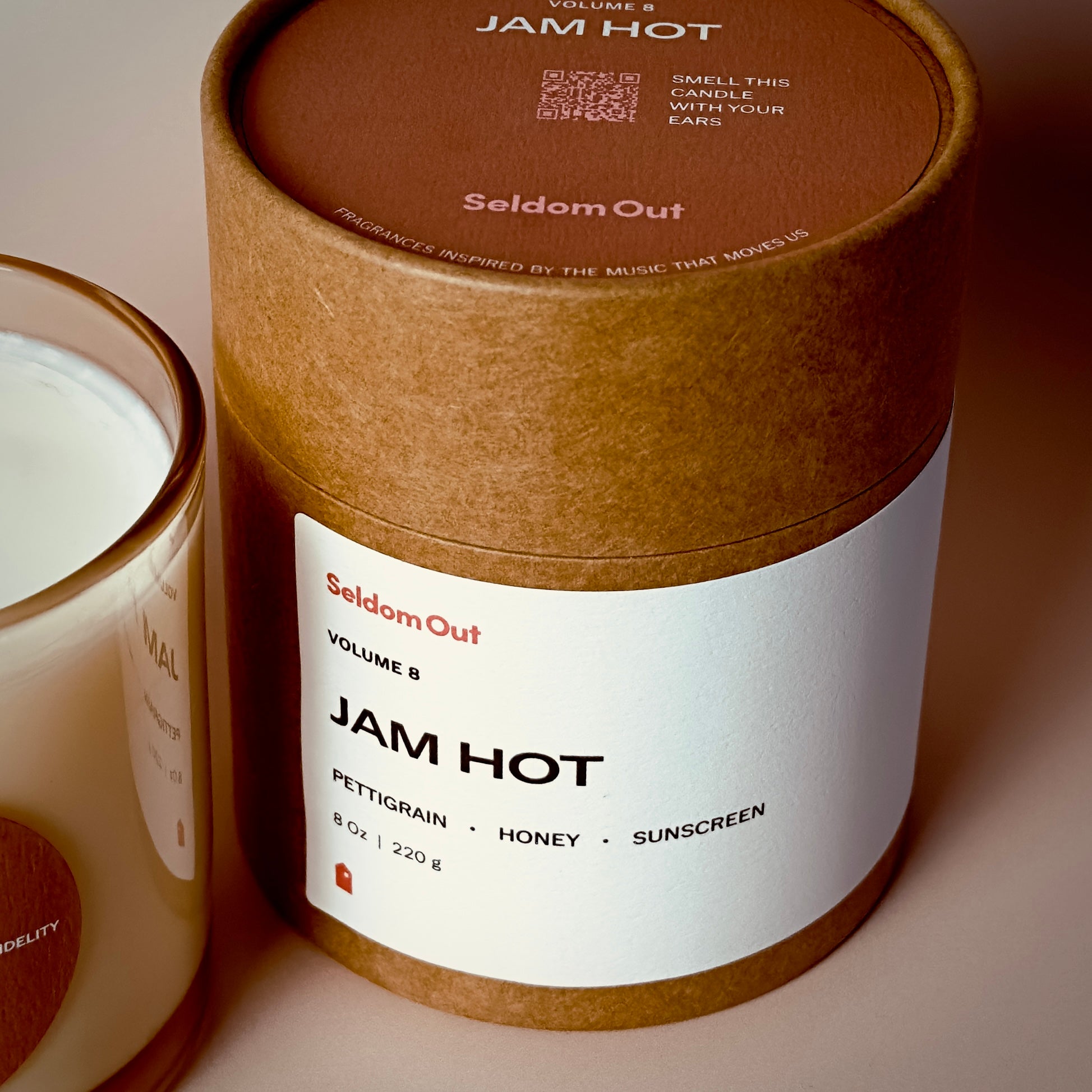 A portrait image of our 8oz Jam Hot scented candle Kraft tube box. It features a wide rectangle label on the front. On the lid is a round label with a QR code that invites you to “smell this candle with your ears”.