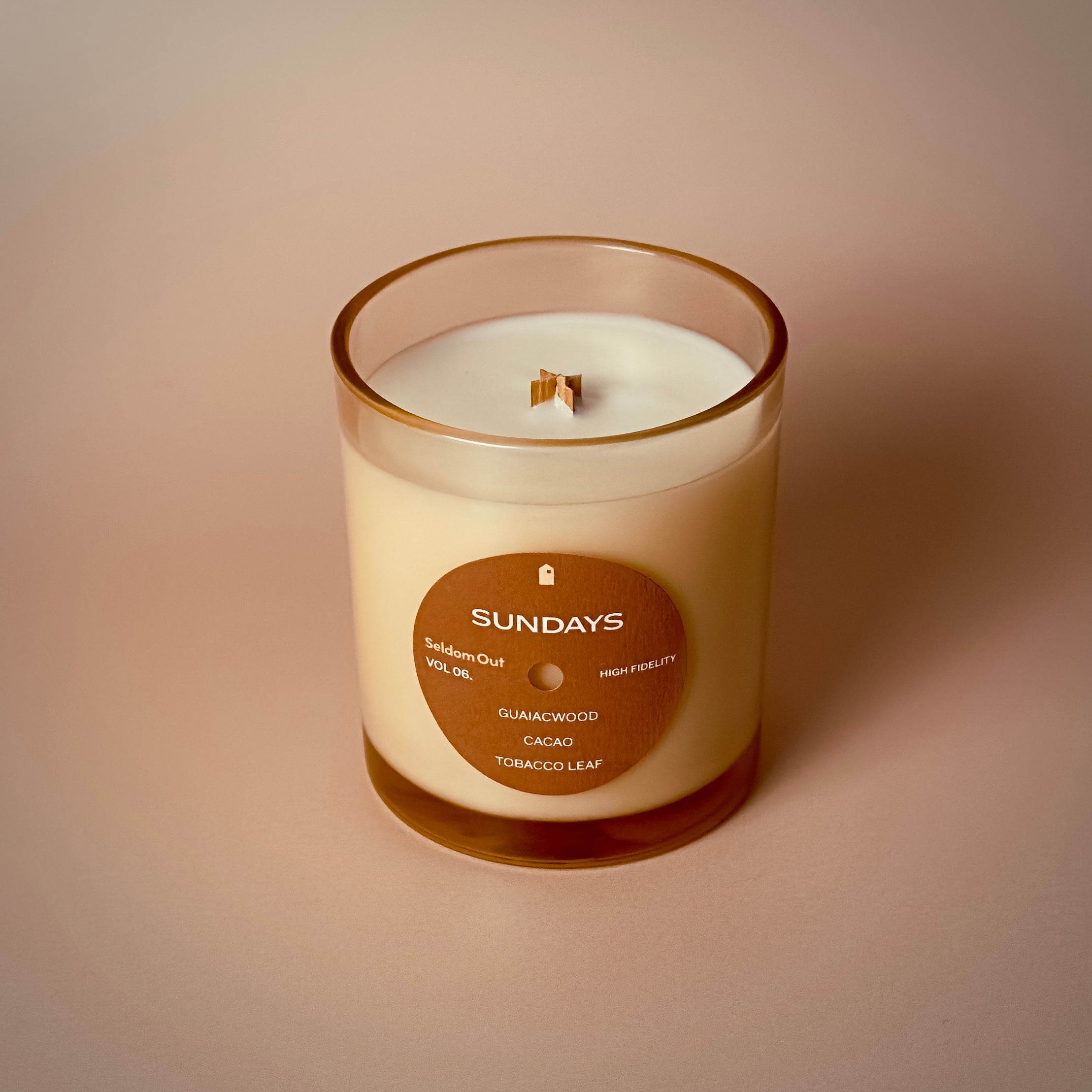 A portrait image of our 8oz Sundays scented candle made in a light amber tinted glass jar. It features a round front label, that has a hole cut out in the middle, not unlike a vinyl record.