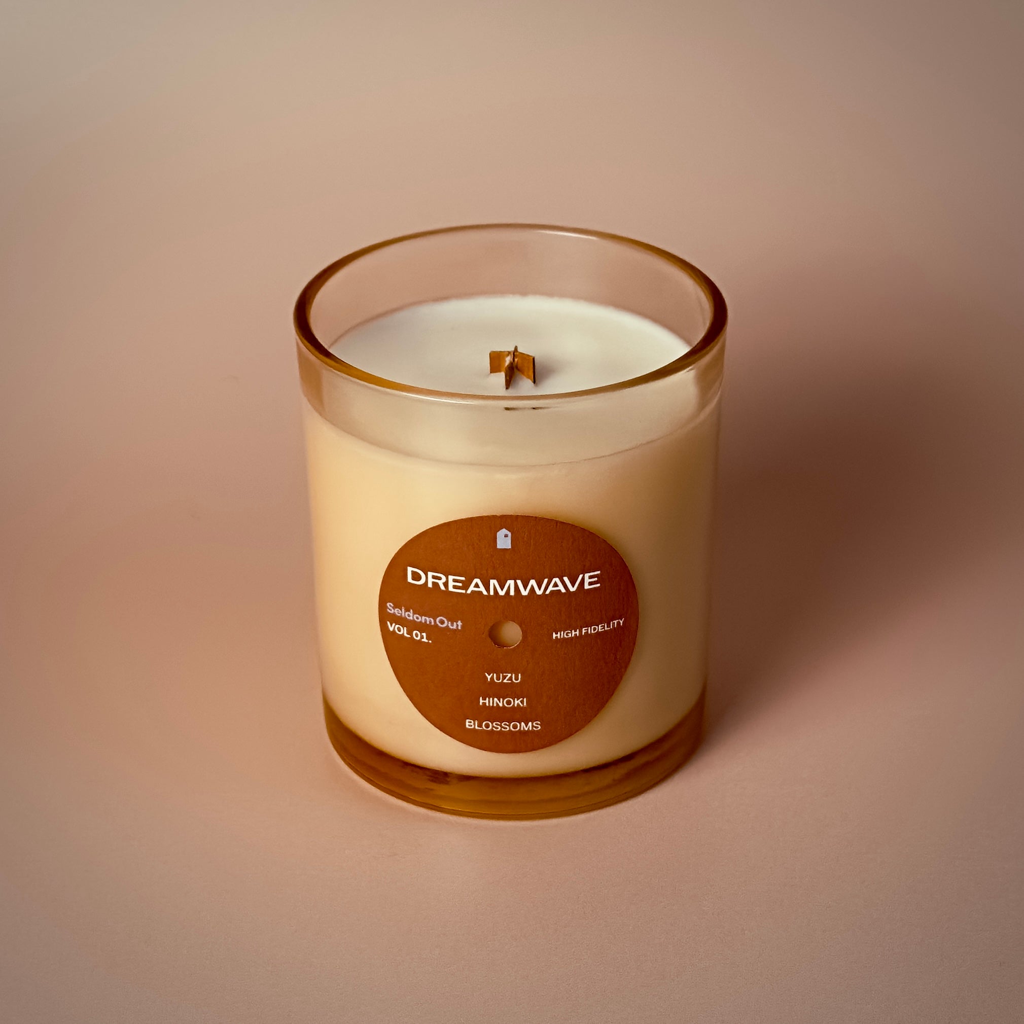 A portrait image of our 8oz Dreamwave candle. It has a slightly brown tinted glass vessel, a round label with a hole at the center, like a vinyl record.