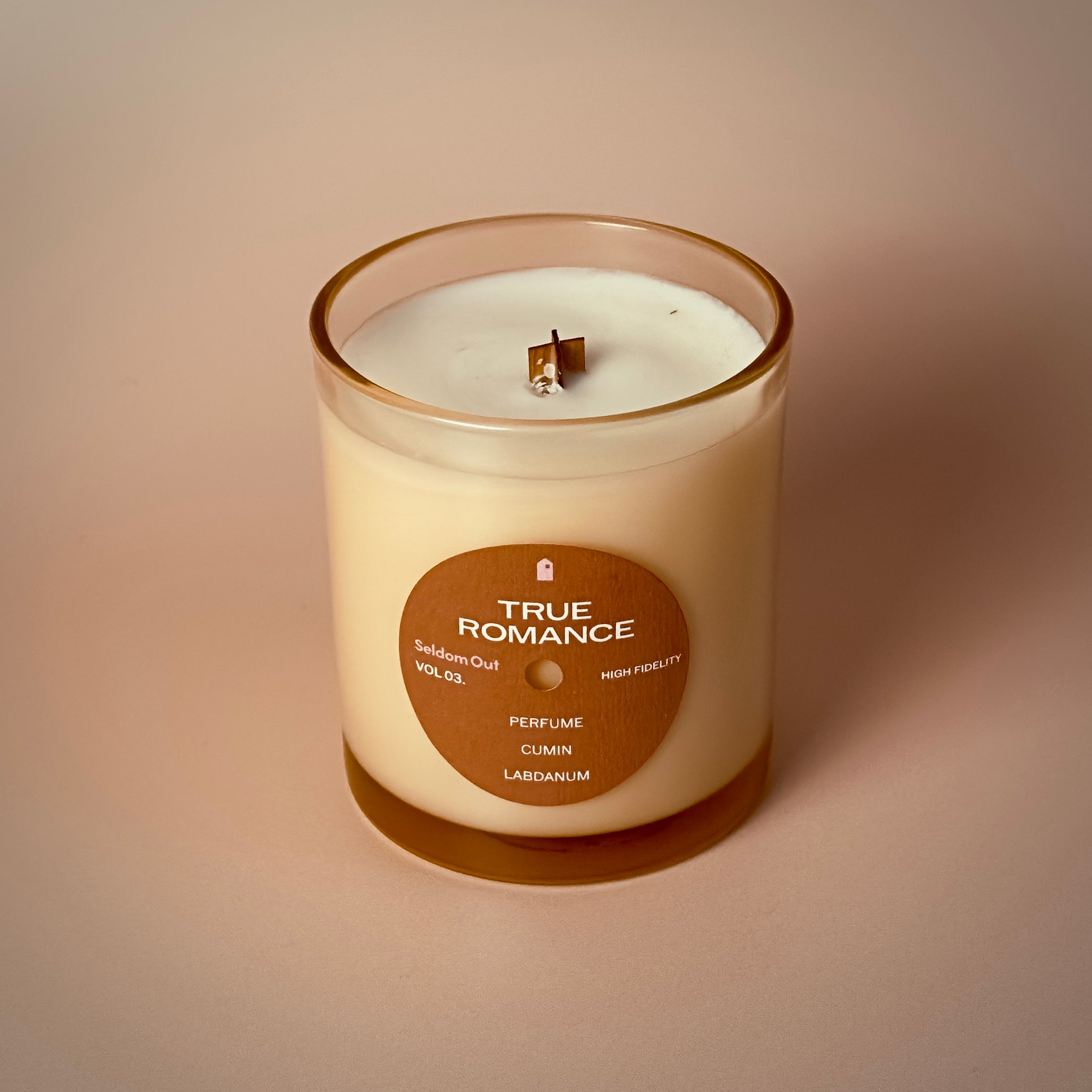 A portrait image of our 8oz True Romance scented candle made in a light amber tinted glass jar. It features a round front label, that has a hole cut out in the middle, not unlike a vinyl record.