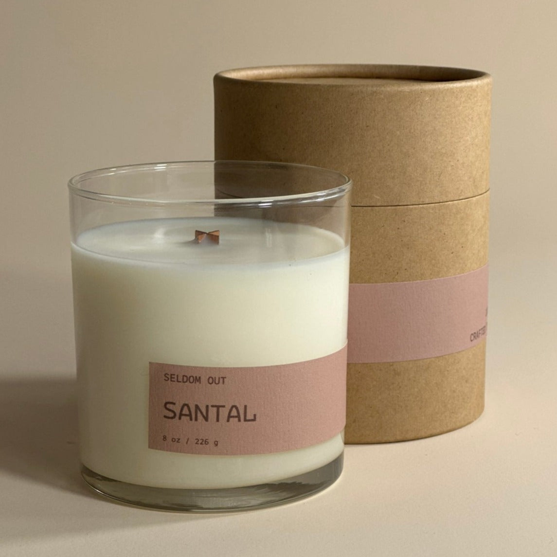 A portrait image of our 8os Santal scented candle made in a clear glass jar. It features a long thin label. Behind the jar stands a Kraft Tube box with a matching label.