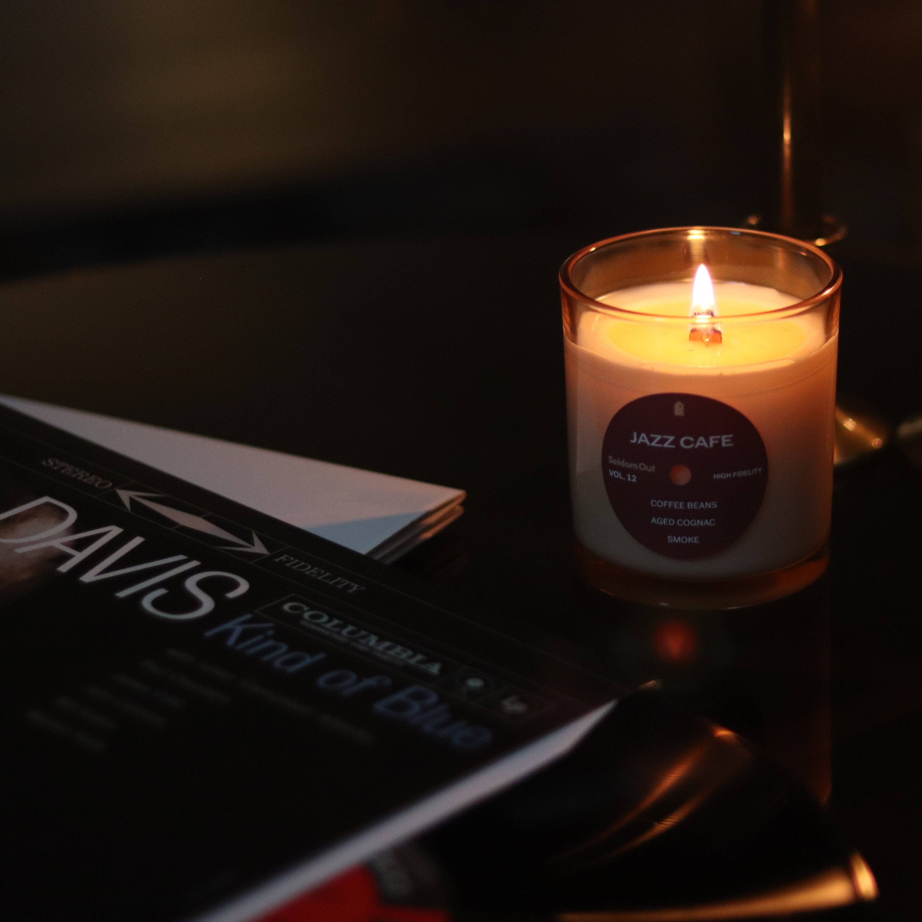 Our 8oz Jazz Cafe sits in a dimly lit scene, the wick is lit casting a bright glow. 