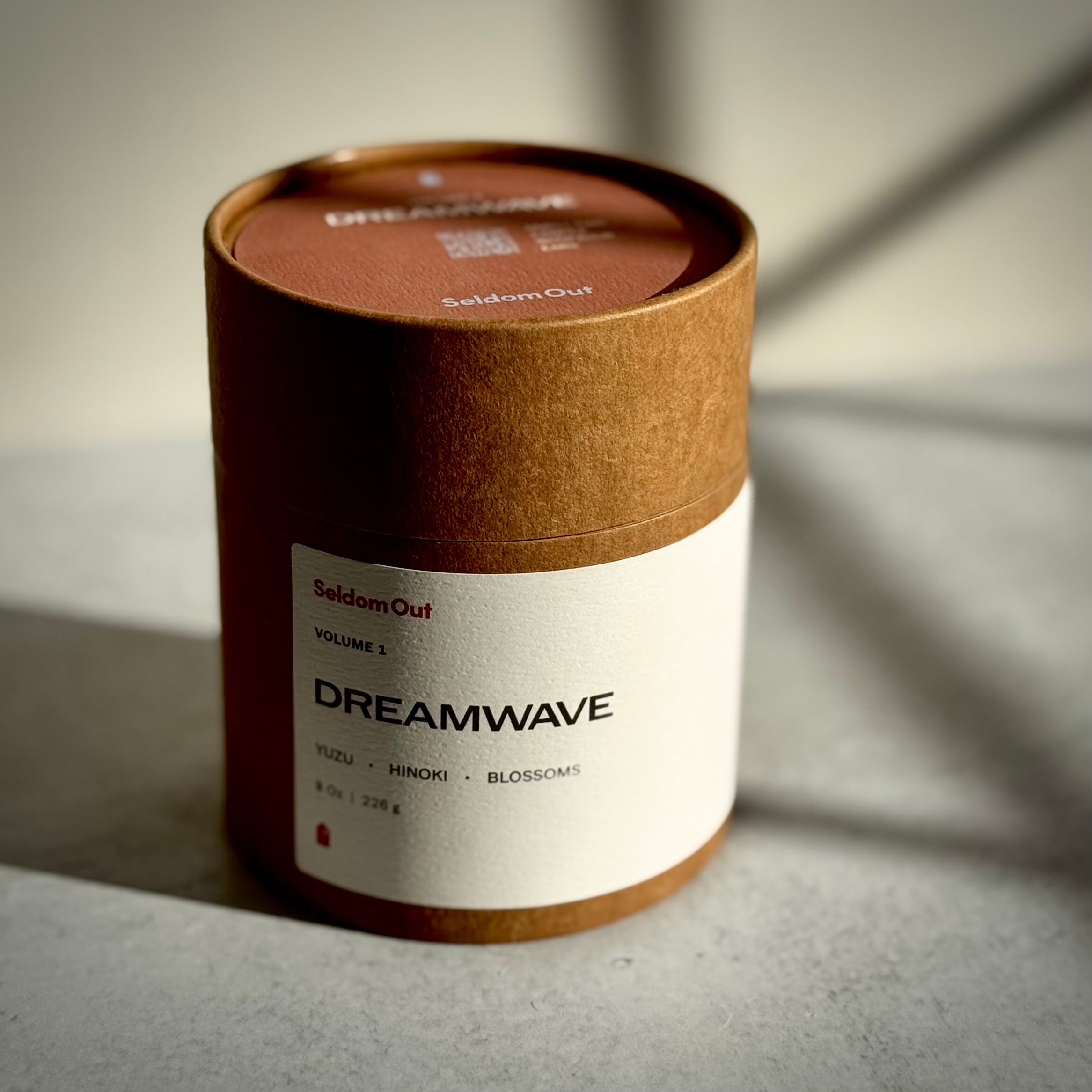A portrait image of our cylindrical product packaging with 'Dreamave' rectangle label on a neutral background with dramatic shadows. The round label on the lid features a QR code that leads to the matching playlist.