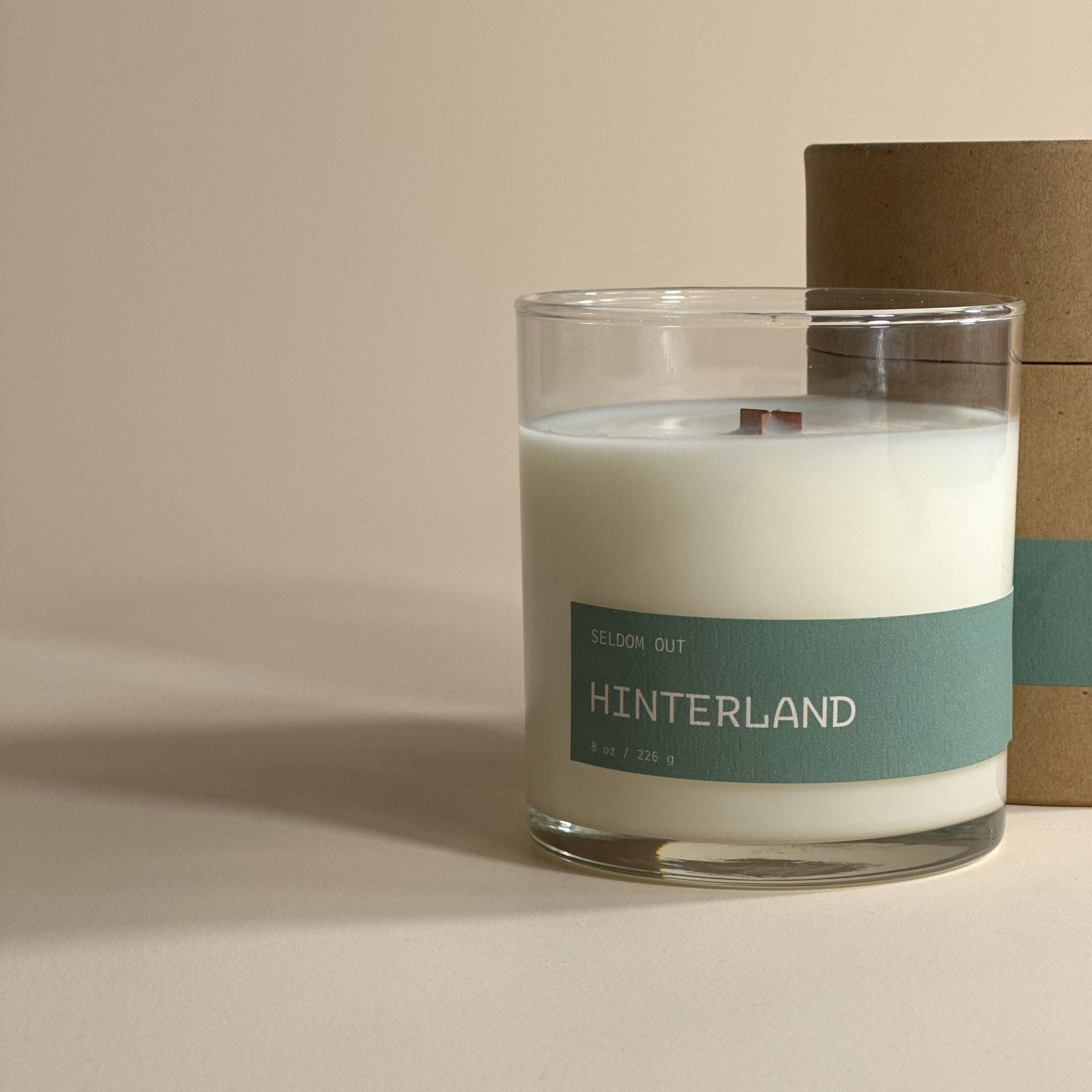 A portrait image of our 8oz Hinterland scented candle, standing in front of its Kraft tube box packaging. Both items feature matching long thin labels that wrap around the width.